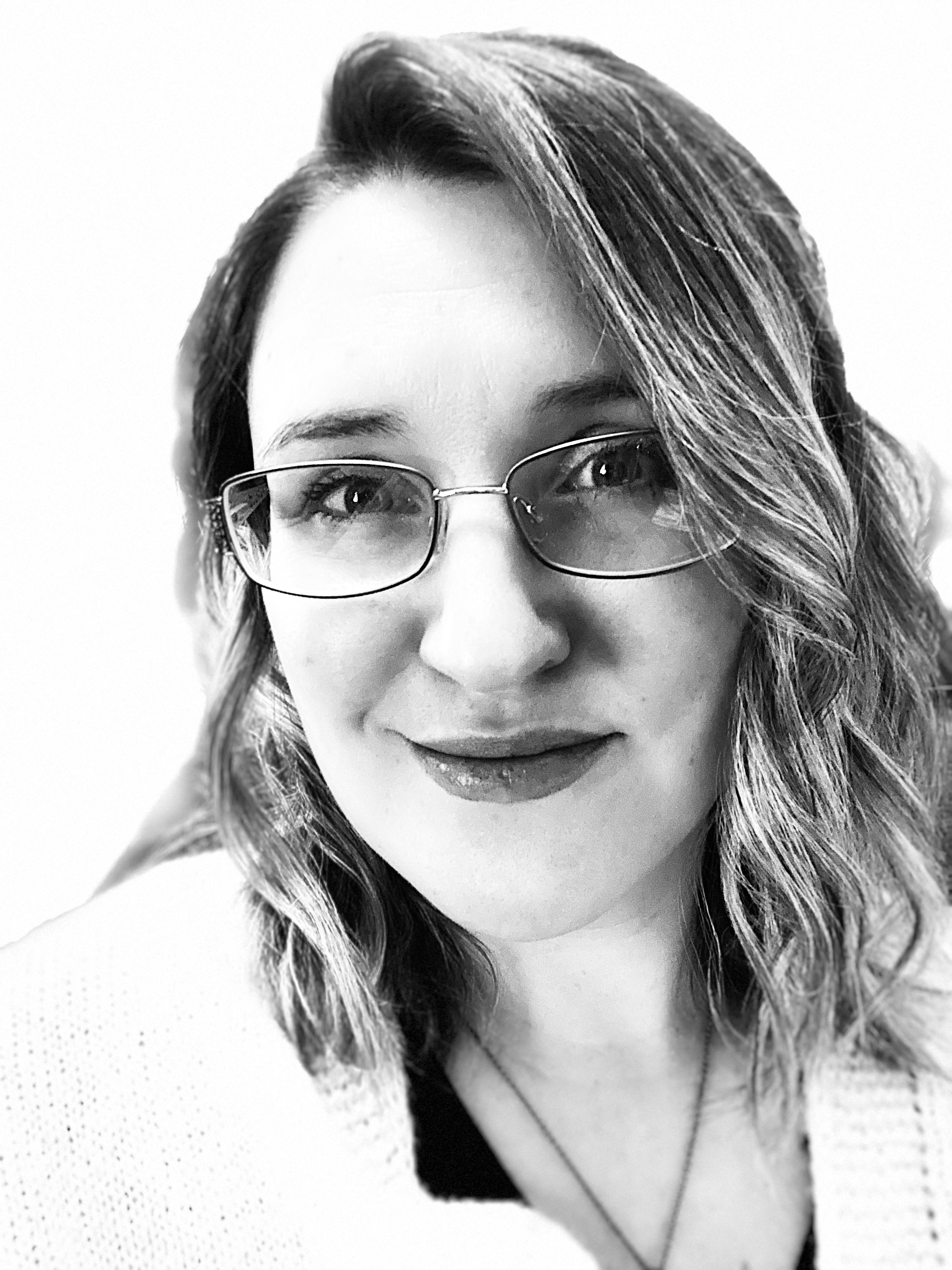 Woman with glasses and wavy hair smiling, looking at camera, in black and white.