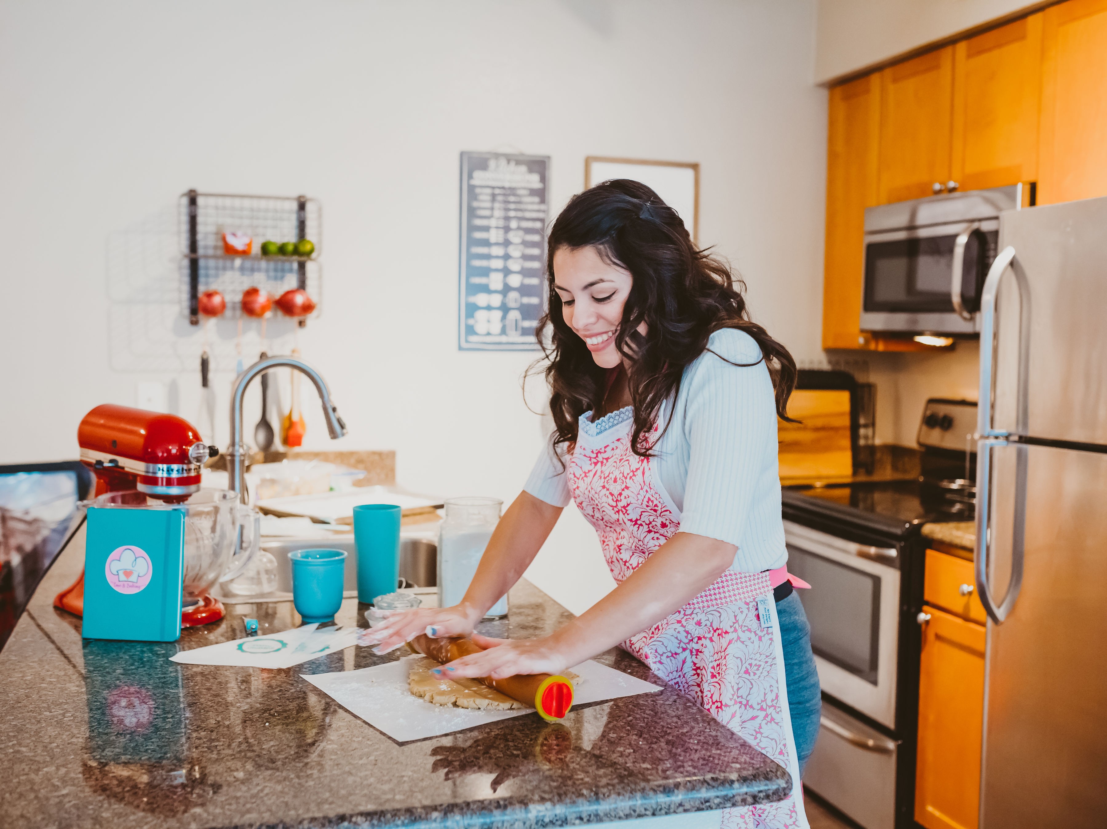 Woman in a kitchen preparing food at a counter with various kitchen items around her.