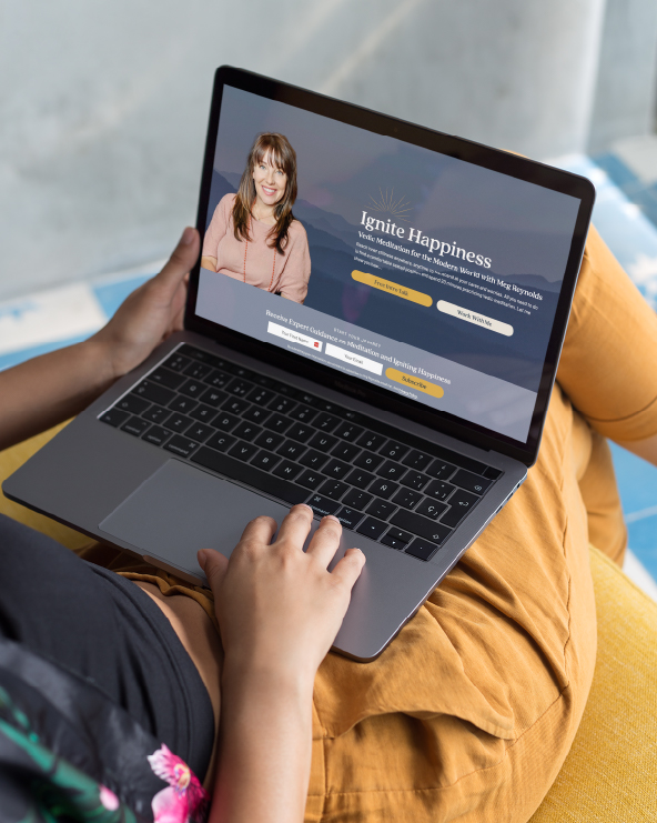 Person using a laptop with a website titled 'Ignite Happiness' displayed on the screen, sitting on a yellow cushion.