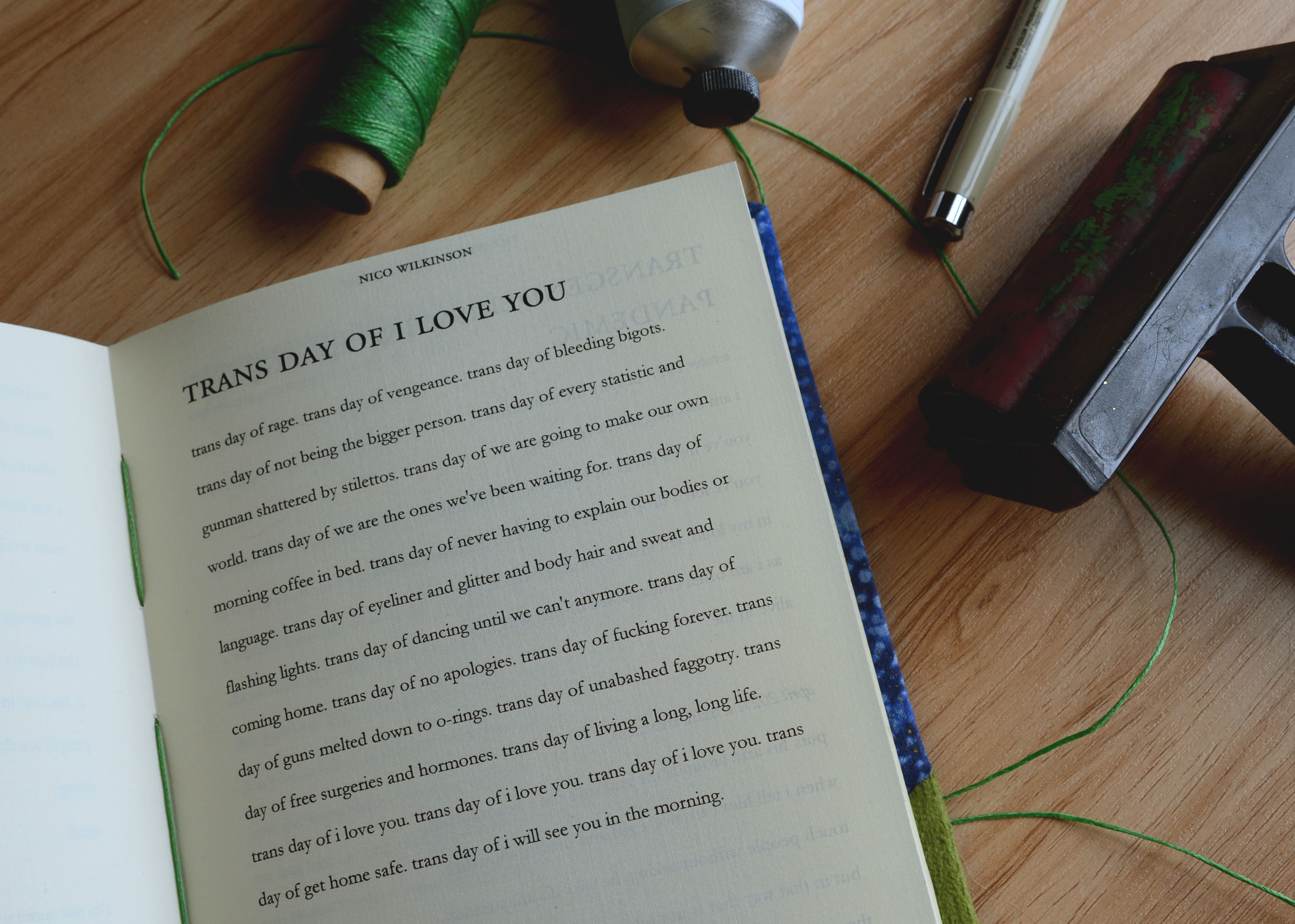 Open book on a wooden table with green thread, pen, and a black object nearby.