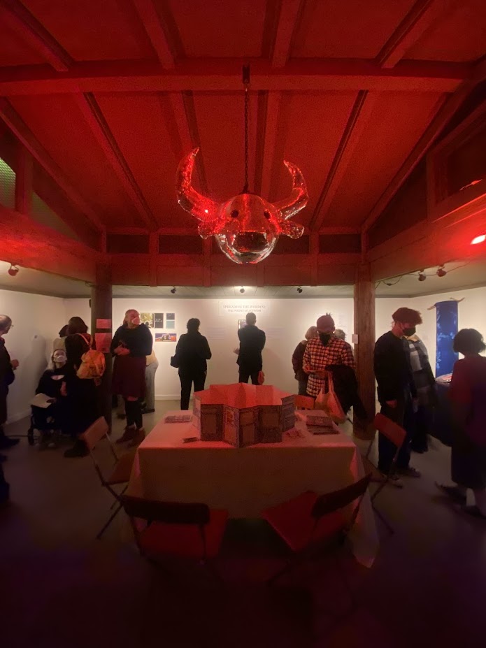 People viewing artwork in a gallery with a red ceiling and chandelier, illuminated by red and white lighting.