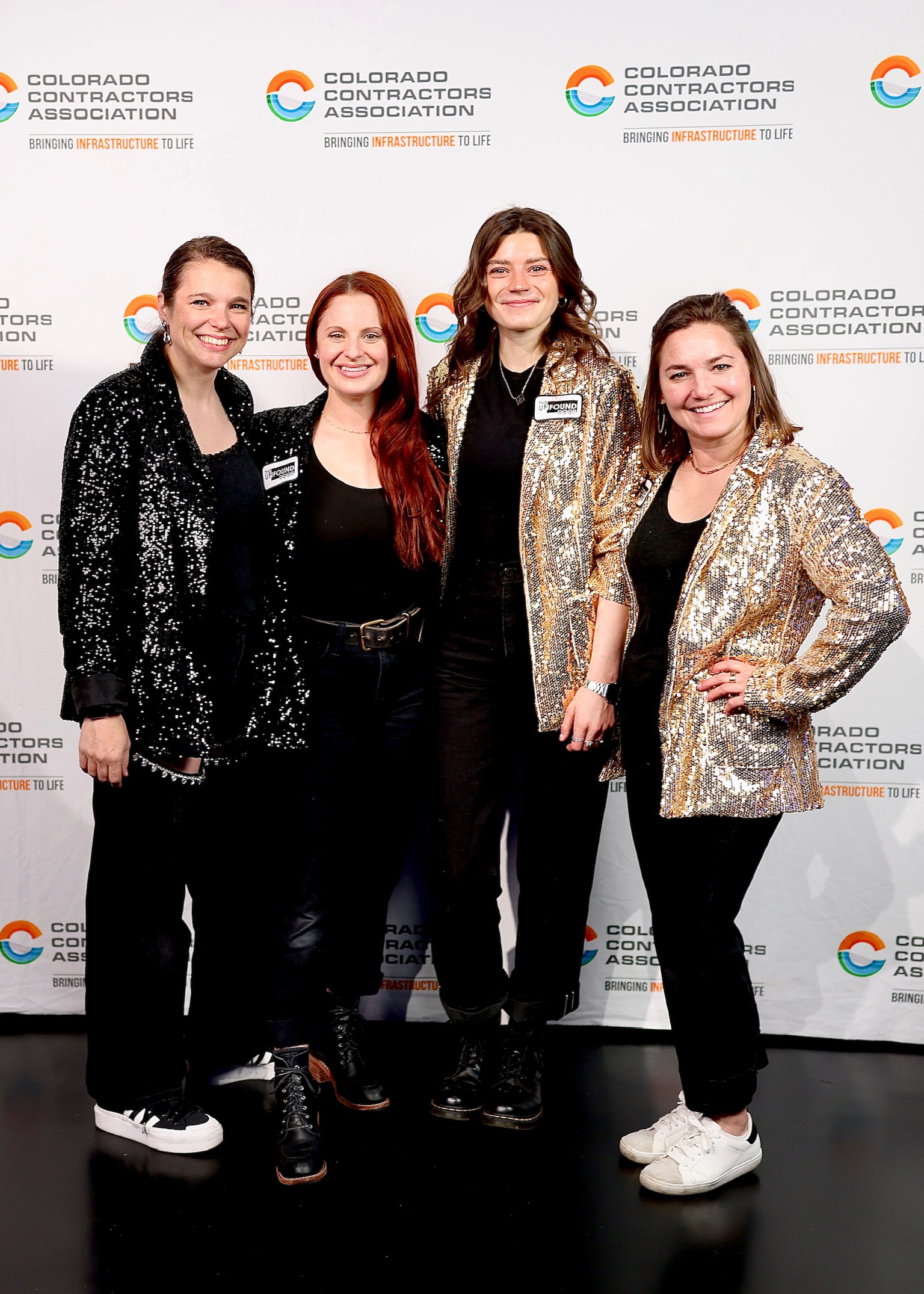 Four women standing together in front of a backdrop with the Colorado Contractors Association logo, smiling and posing for the photo.
