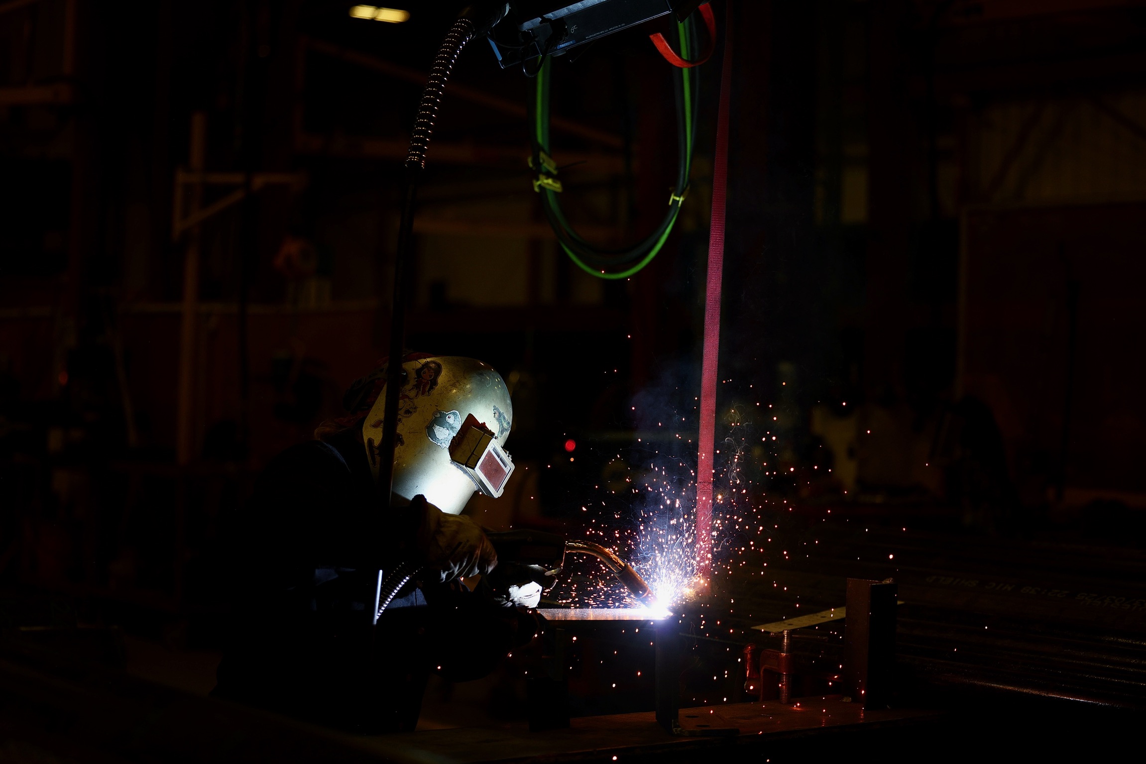 Person welding with bright sparks and protective gear in a dark industrial setting.