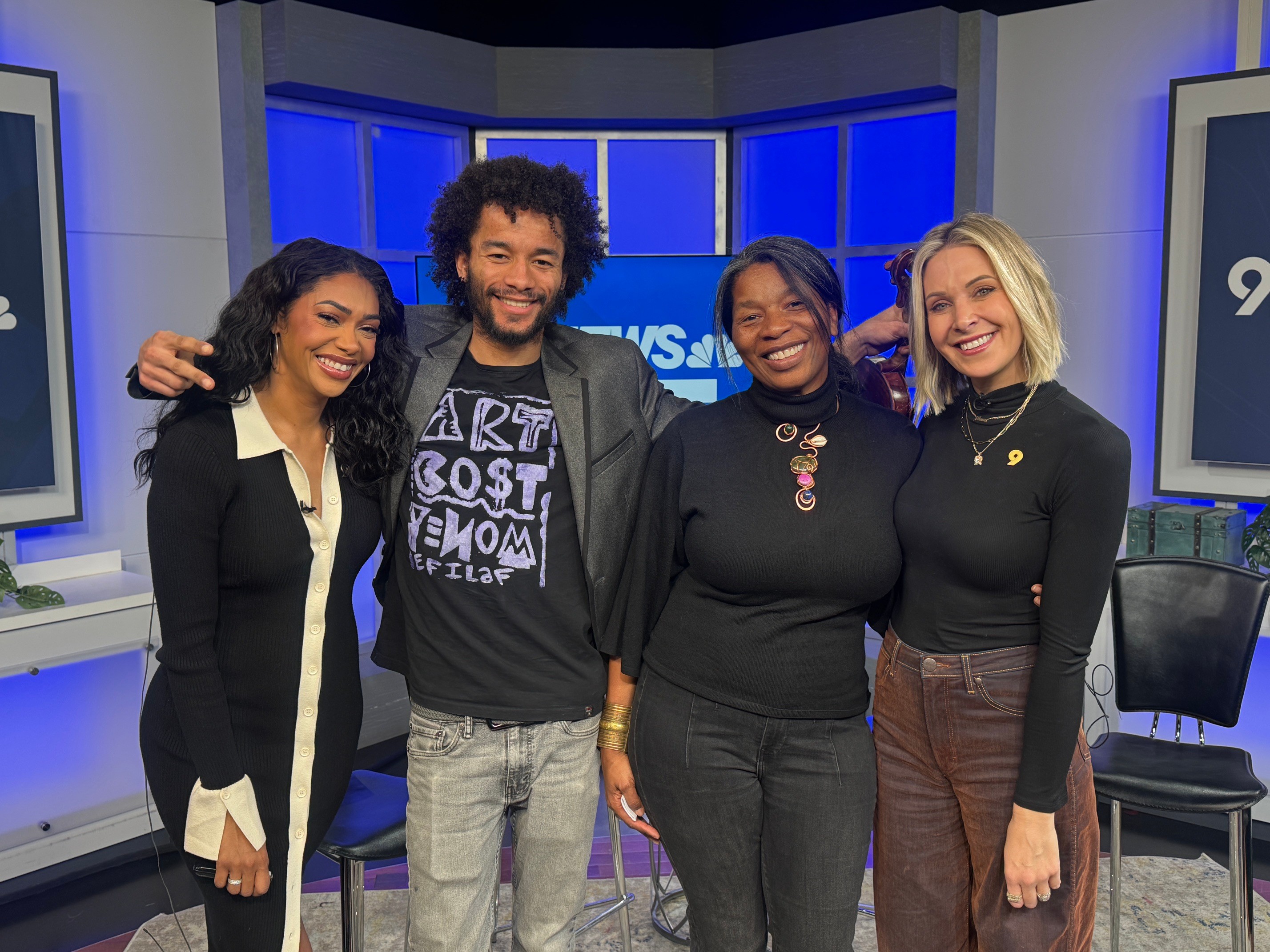 Four people smiling in a TV studio, standing close together with arms around each other.