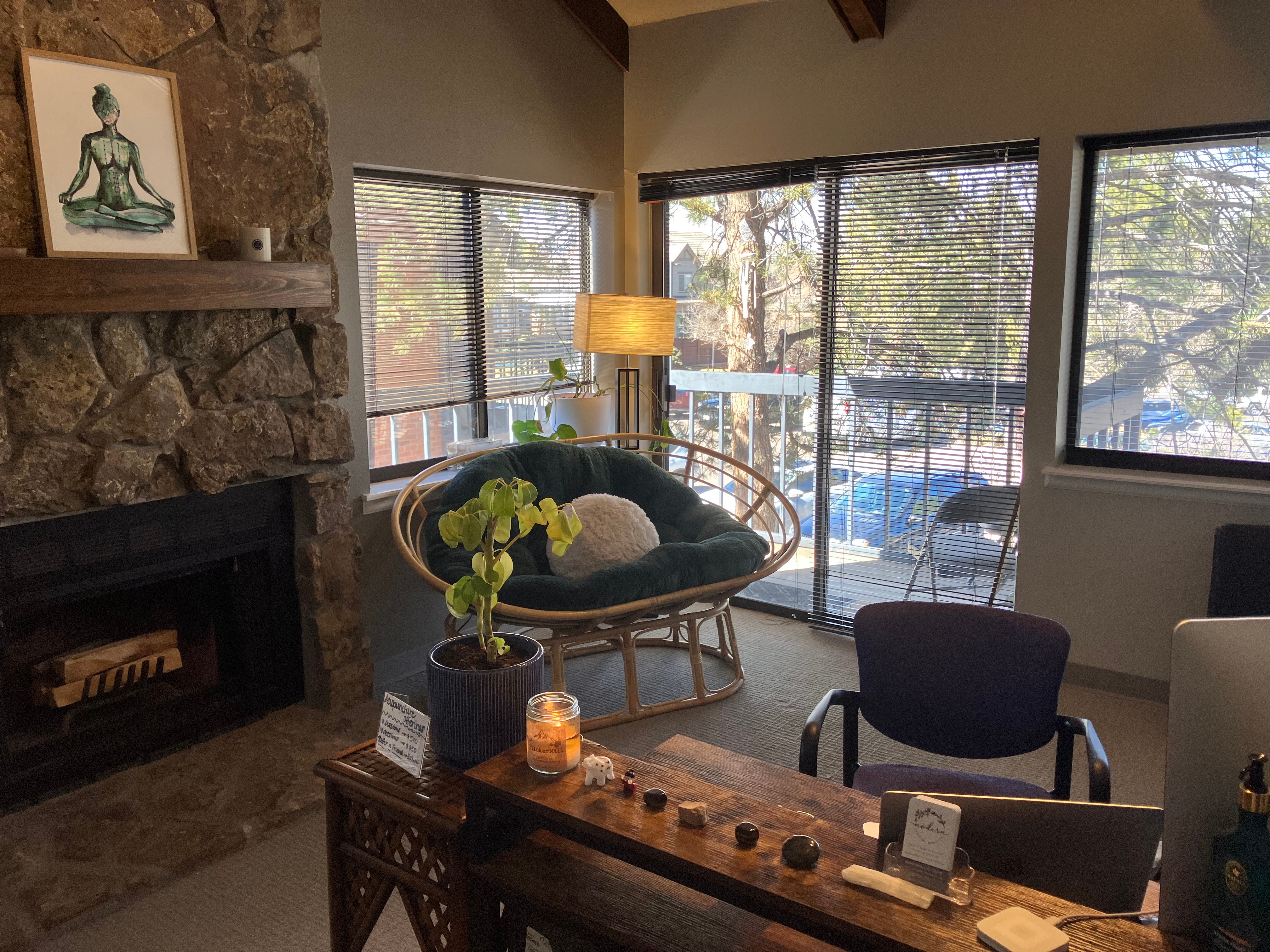 Living room with large windows, stone fireplace, wicker chair with cushions, and a wooden table with decorative items.