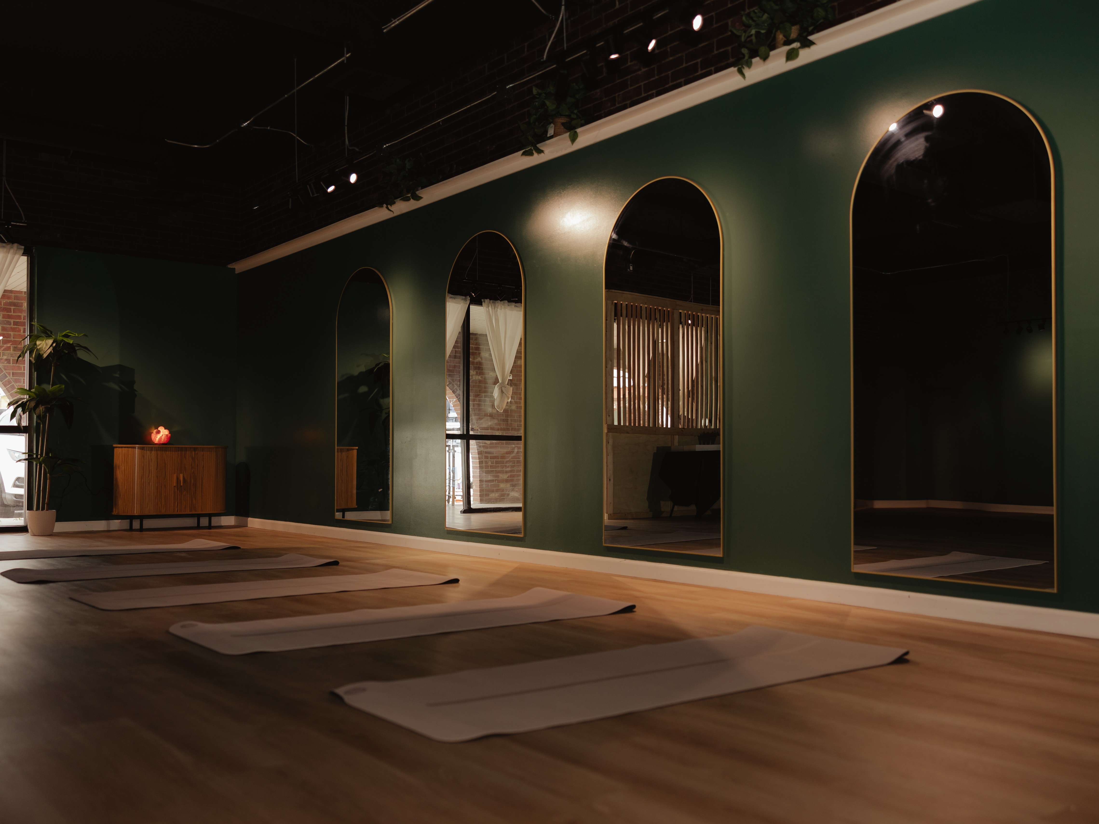 Room with green walls, four large arched mirrors, wooden floor, and yoga mats on the floor.