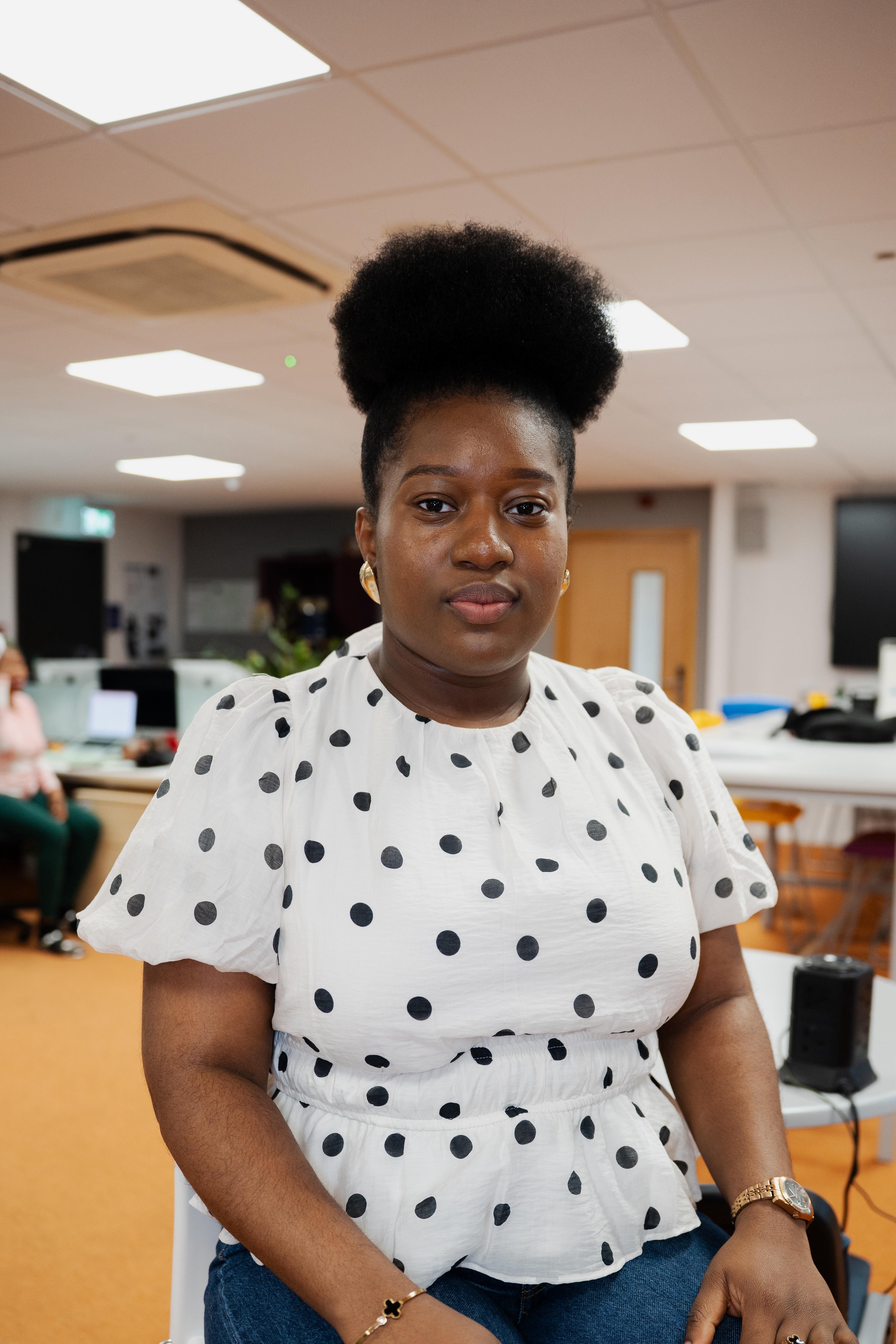 Woman with natural hair in a polka dot blouse standing in an office environment.
